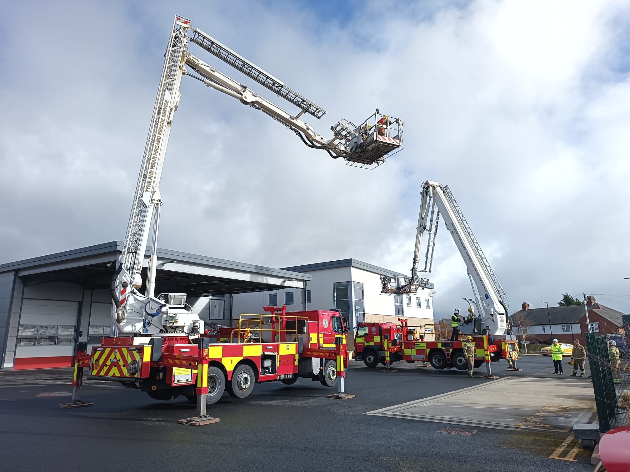 Photograph of two fire service vehicles with aerial ladder platforms extended high into the sky