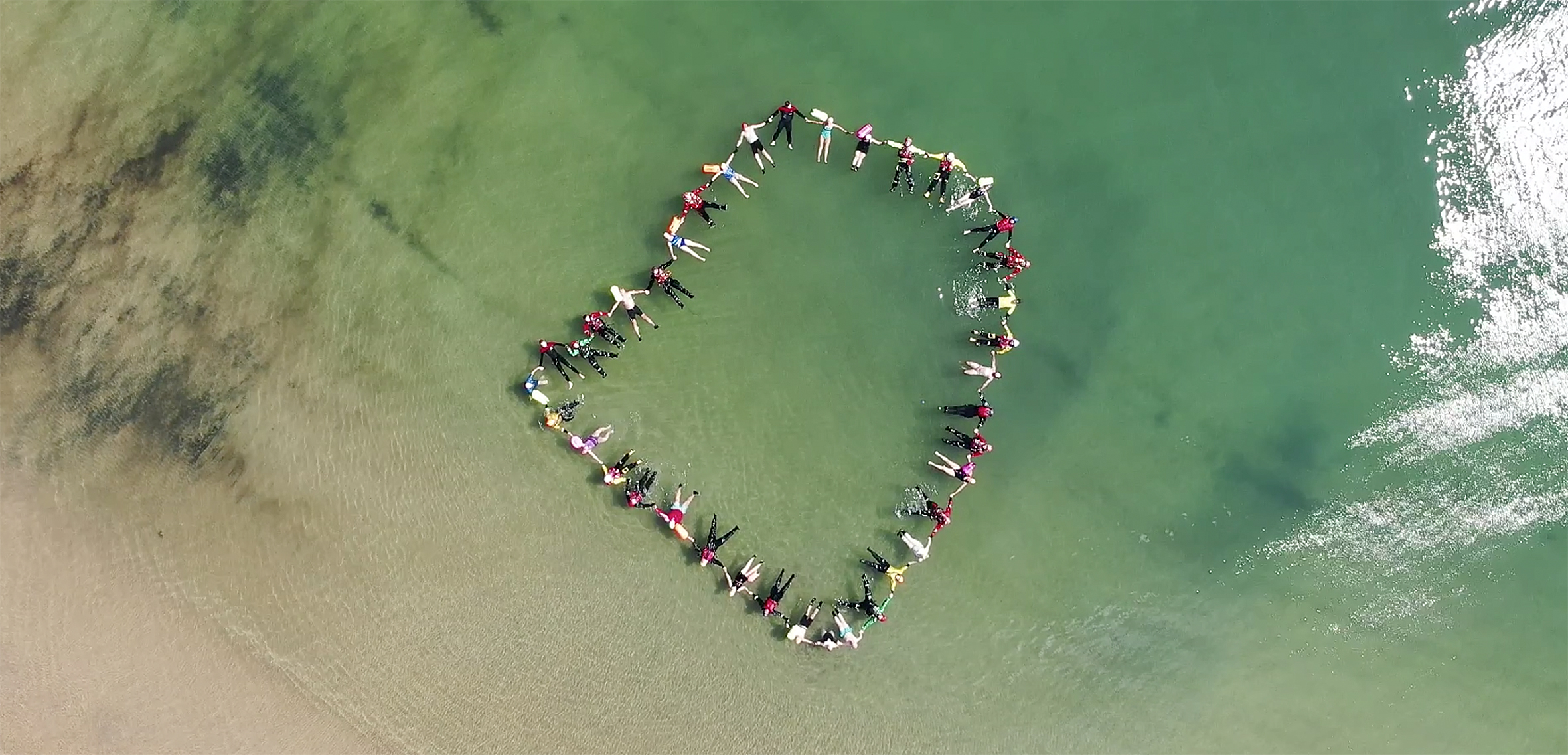 A large group of wild swimmers holding hands, floating in the sea