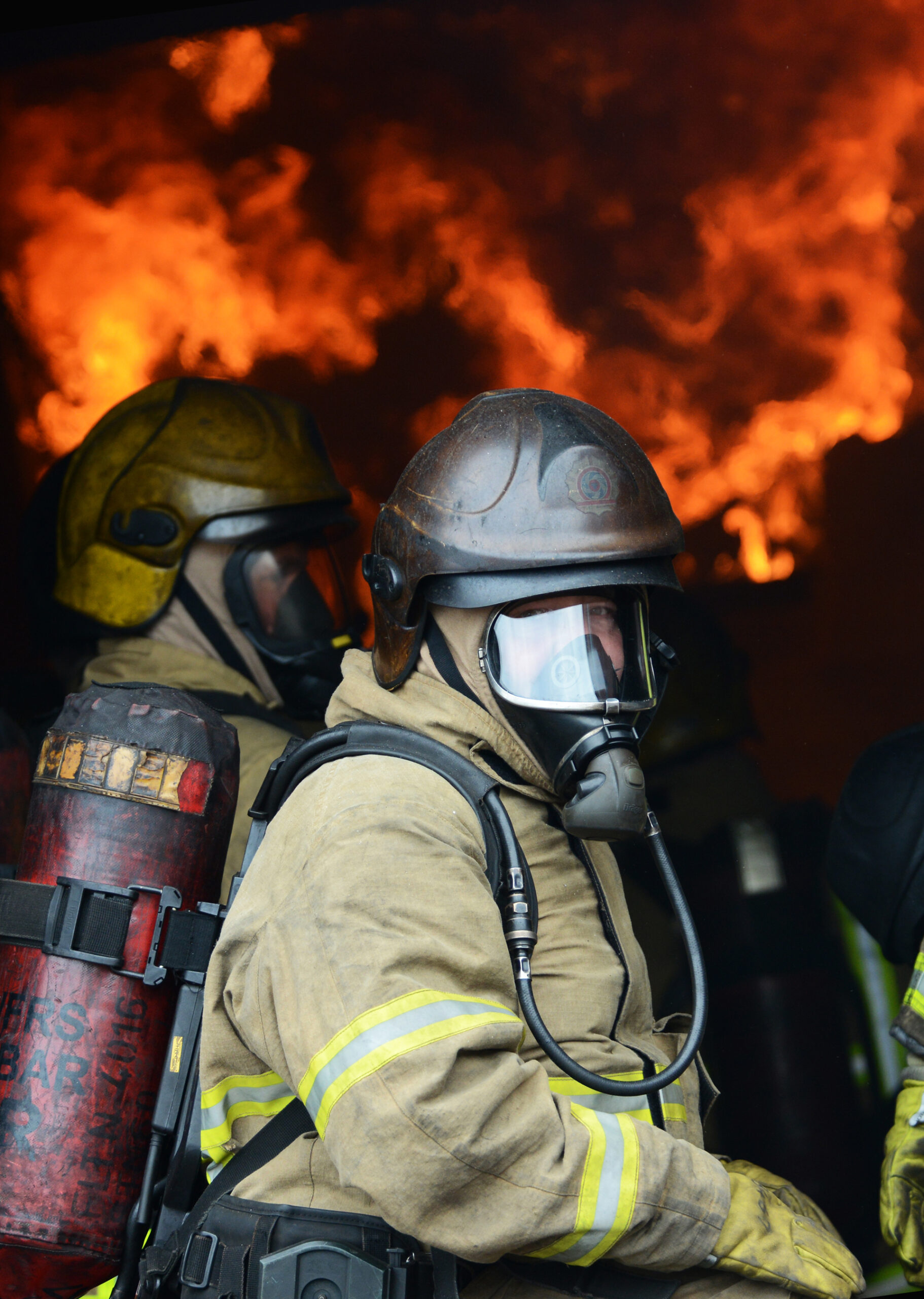 Photograph of a firefighter wearing breathing apparatus with a fire behind him