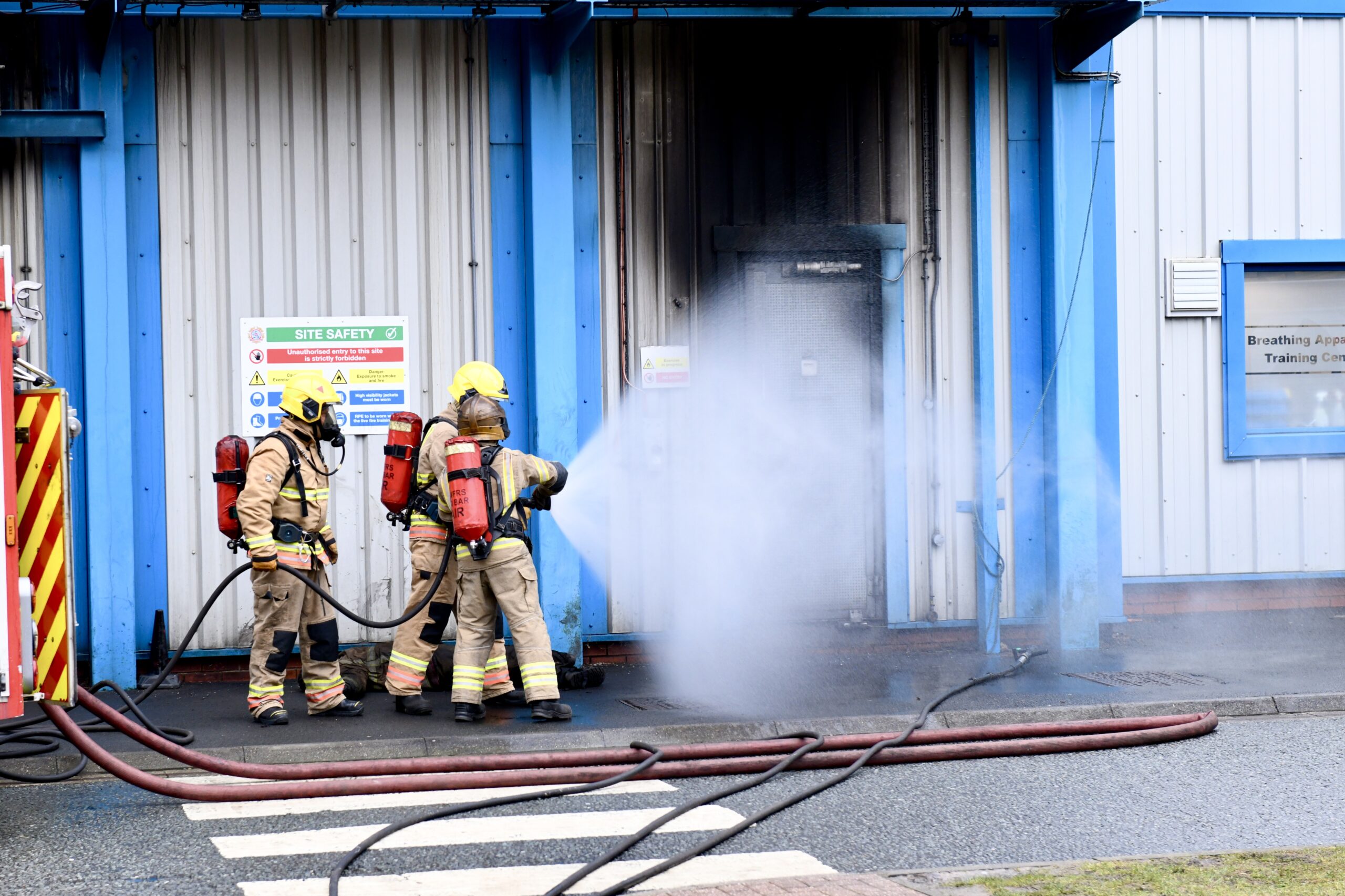 Three firefighters, holding a hose, wearing full PPE including breathing apparatus