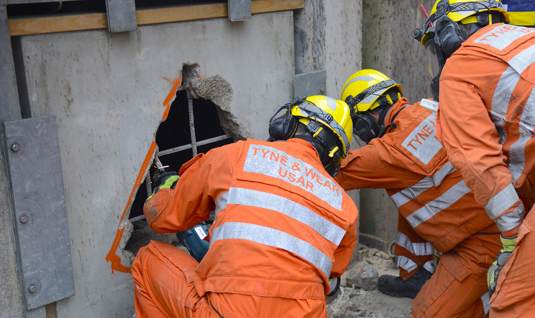 Photograph of the urban search and rescue team using equipment to break through a solid concrete wall
