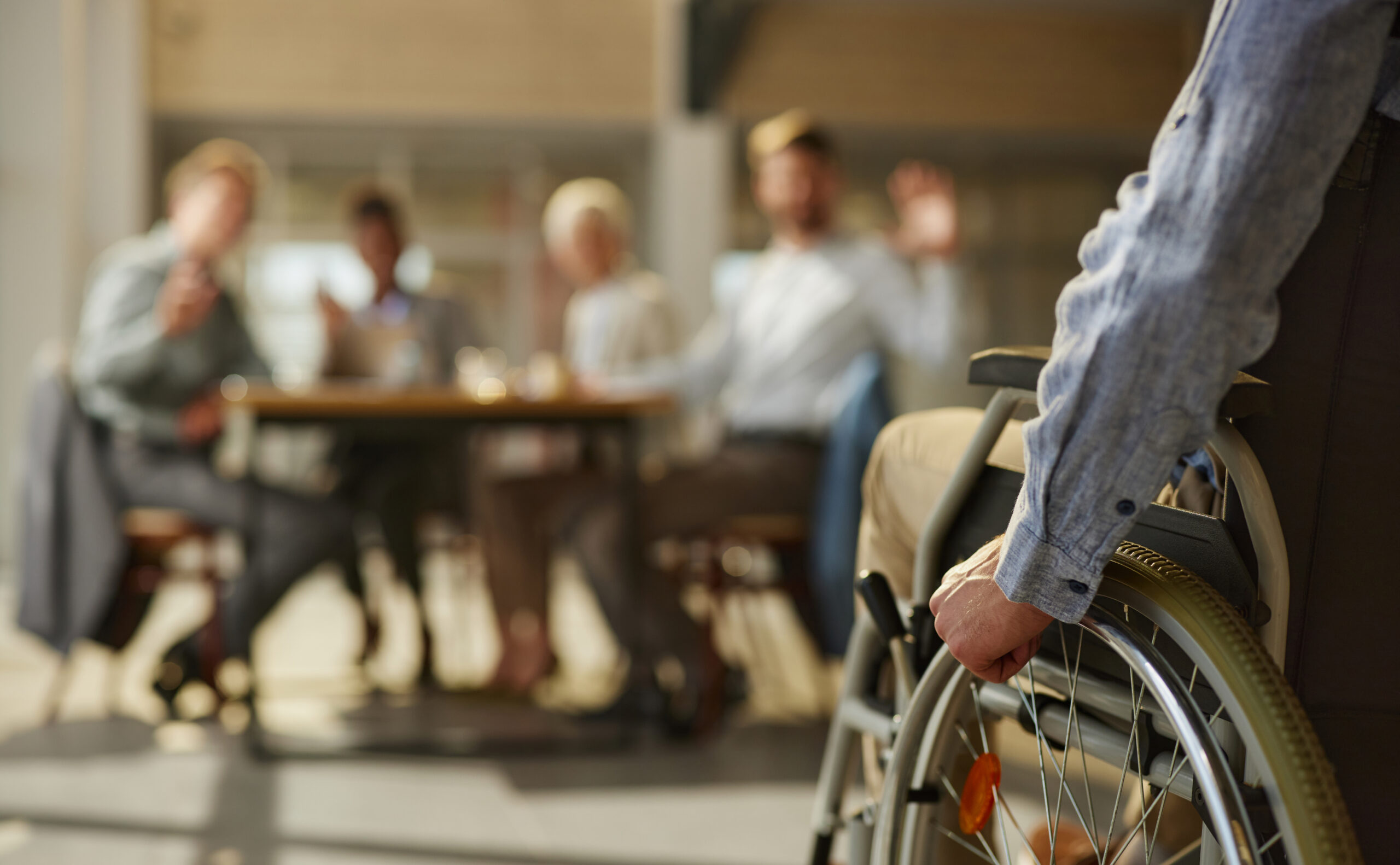 A photograph of a person in a wheelchair positioned to the right of the picture with the arm and side of the wheelchair in view. Background is blurred.