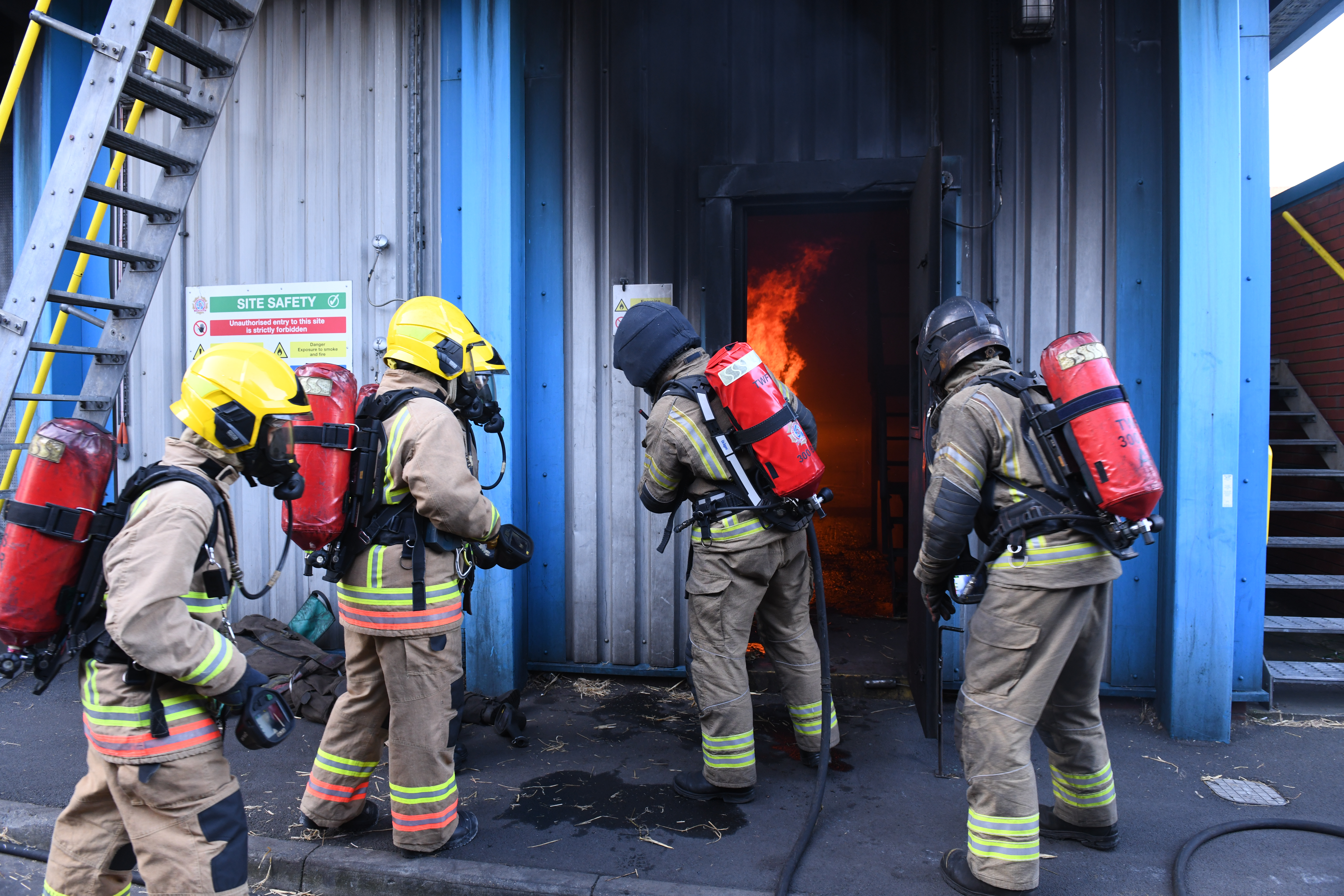 Photograph of four firefighters, wearing breathing equipment, entering a burning building