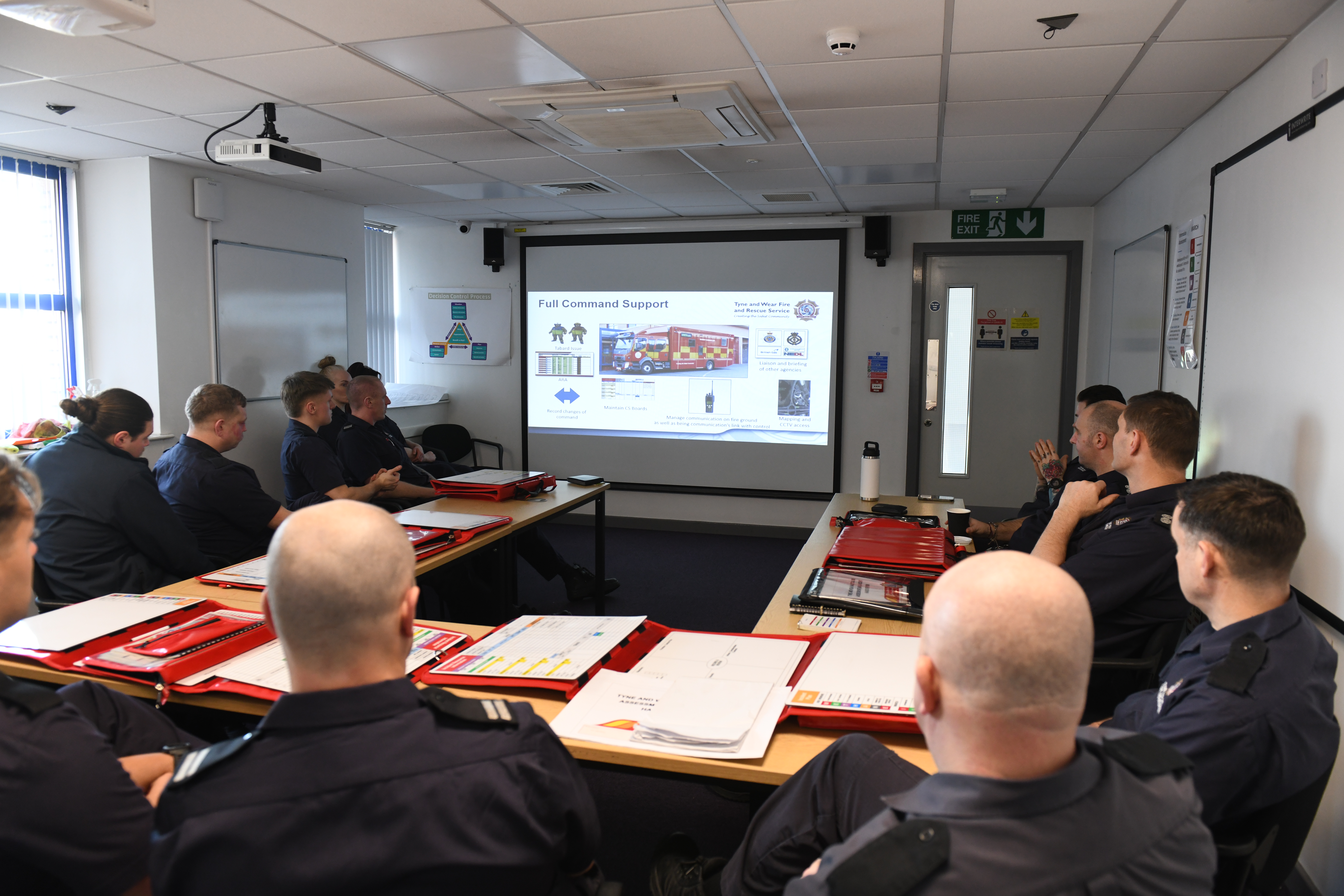 Photograph of a room full of firefighters sitting viewing a presentation screen, in a class room