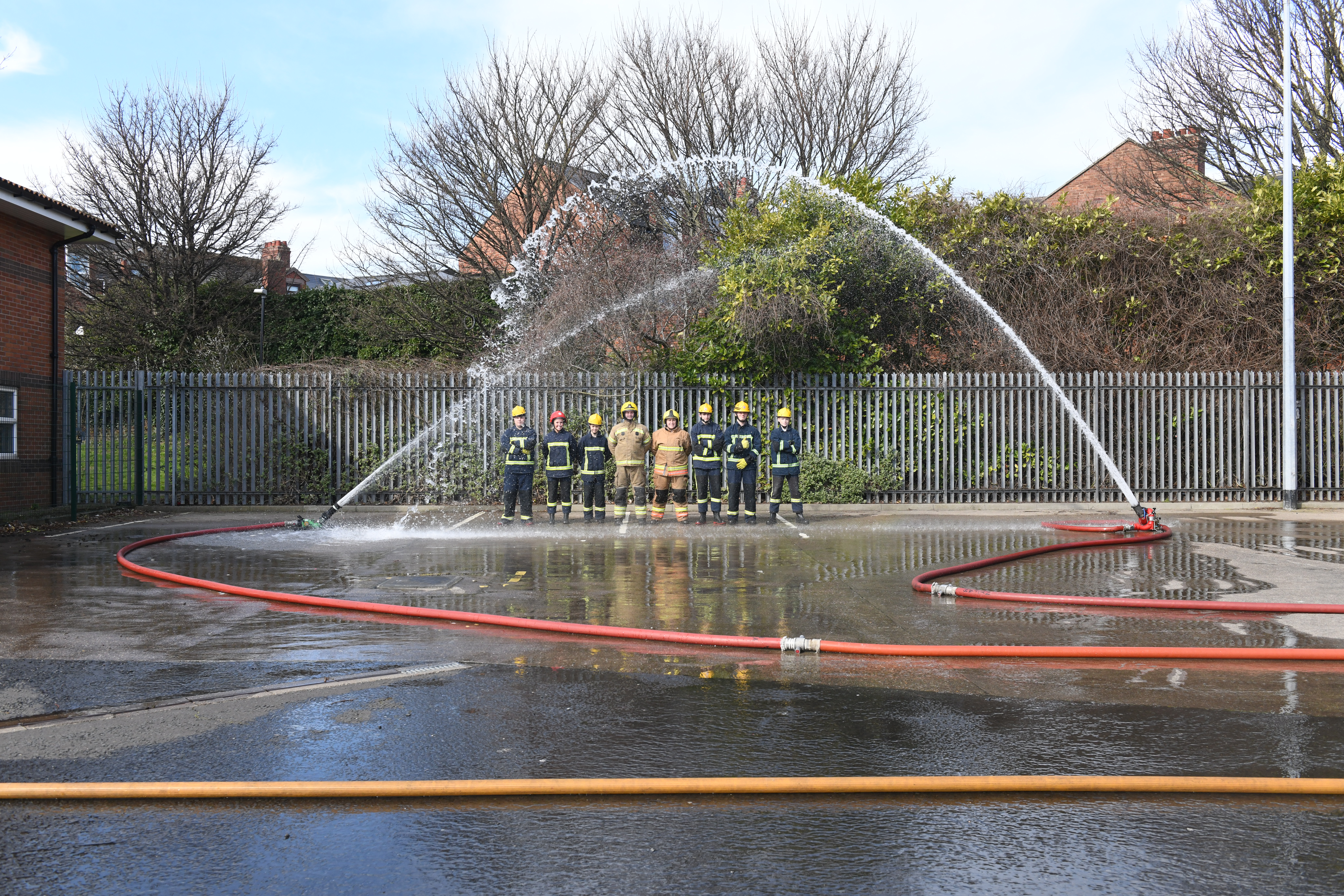 Photograph of a group of young people in fire kit standing under a hose