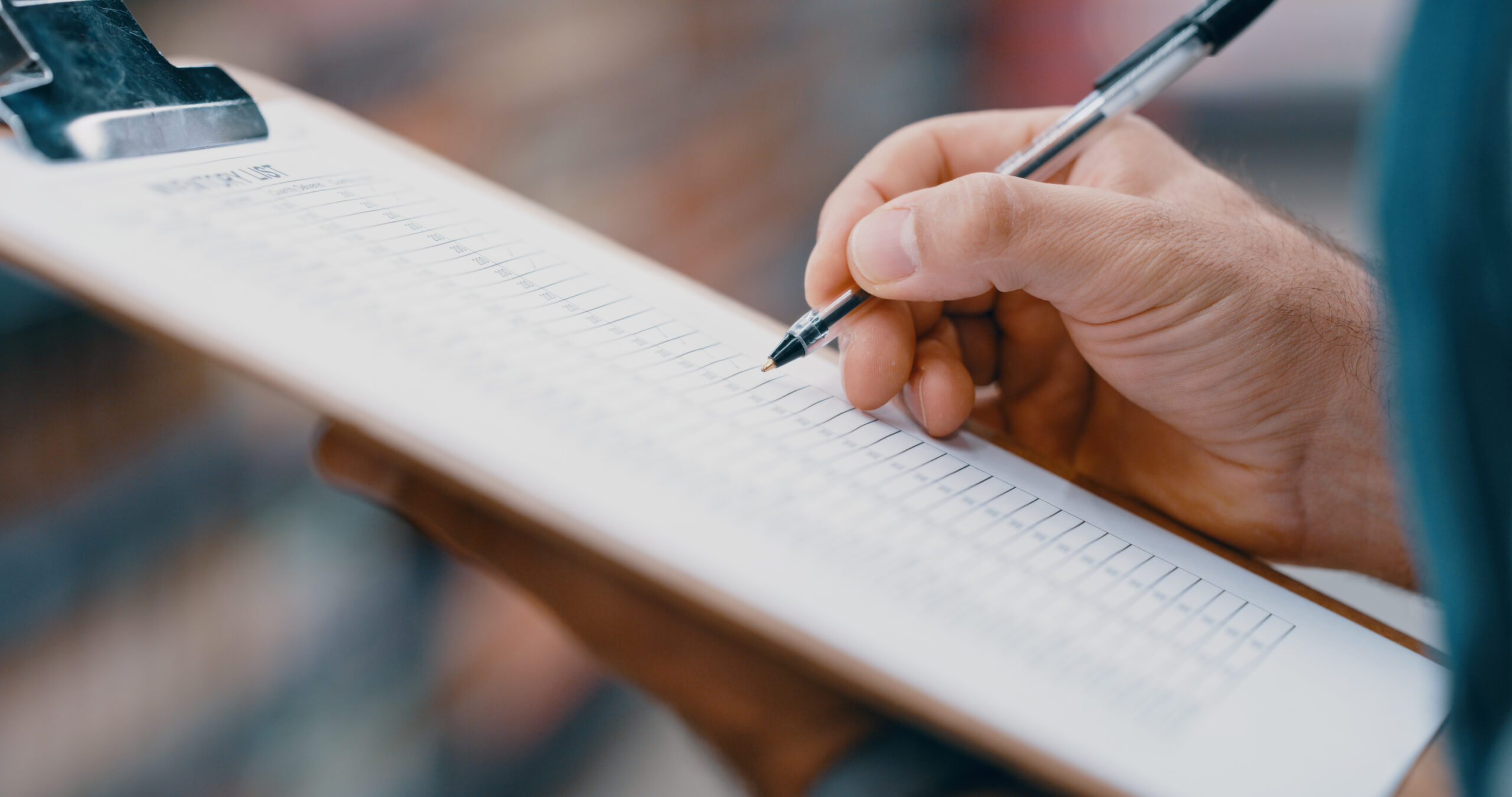 Hands holding a pen writing information on to a clipboard.