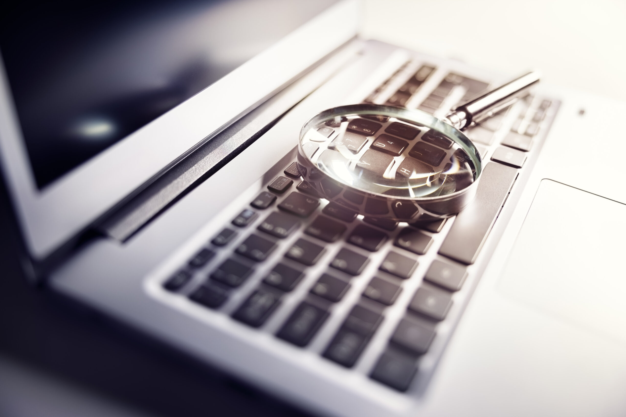 Governance - a computer with a magnifying glass placed over the keyboard