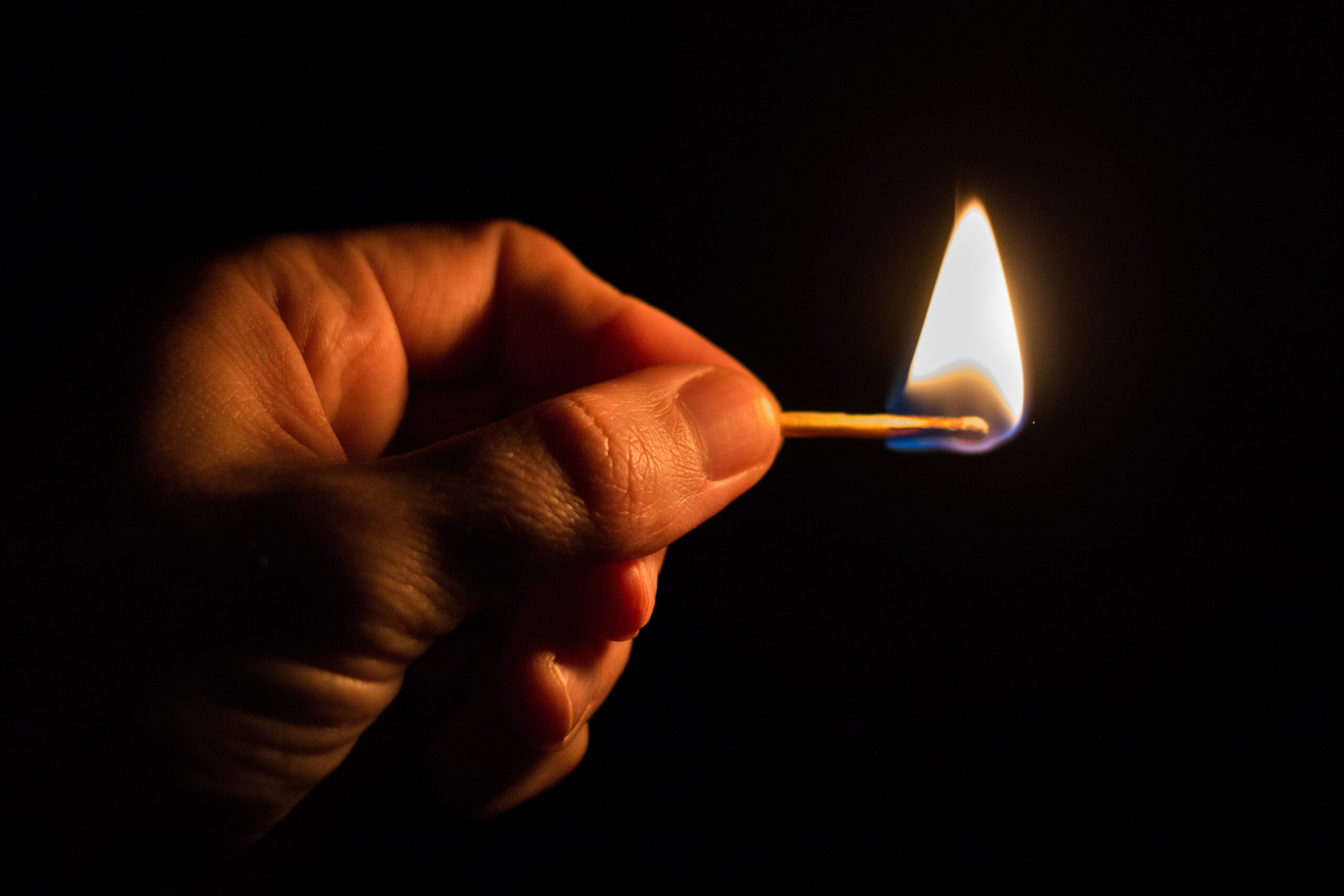 A finger and thumb holding a single match that is a light.