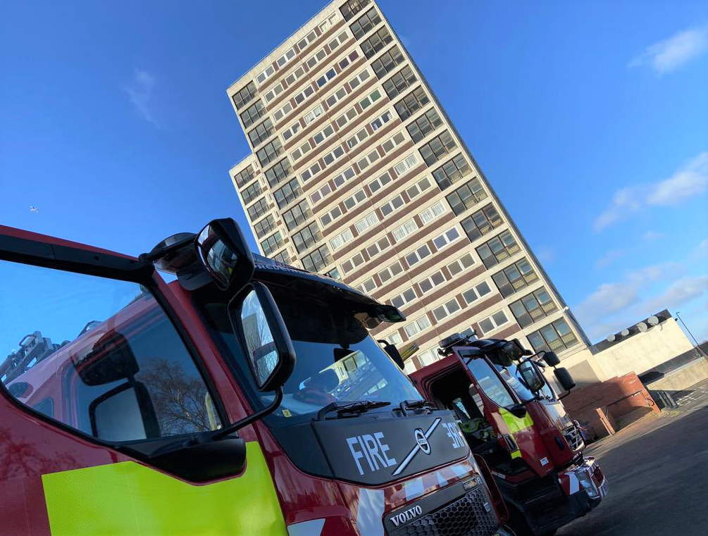 Two fire appliances parked outside of a highrise building.