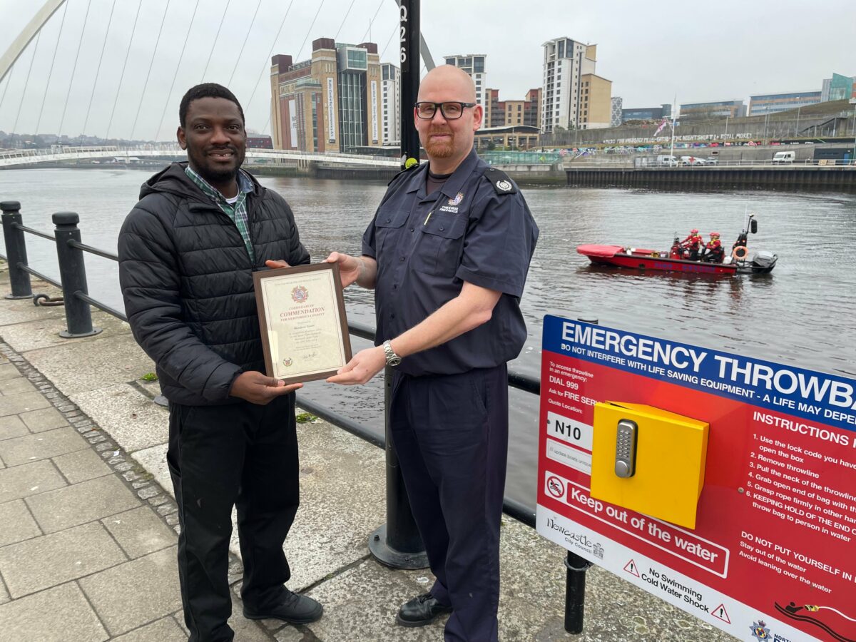 Photograph of security guard being presented with a certificate, standing with a fire officer on a river bank