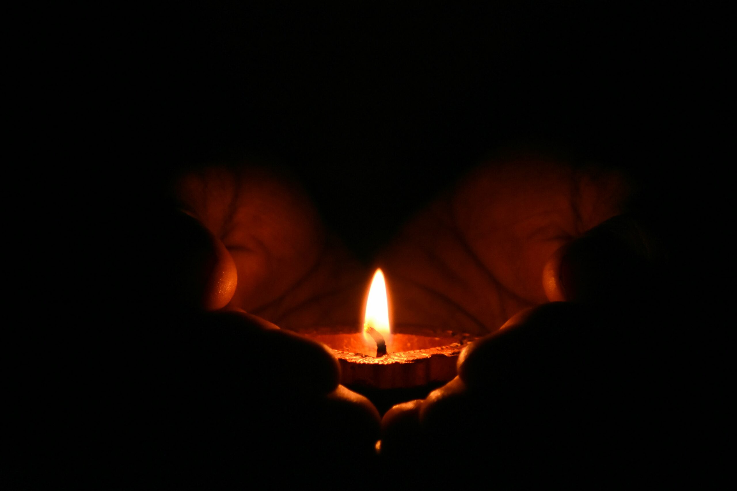 Hands holding a diya oil lamp with a lit wick.