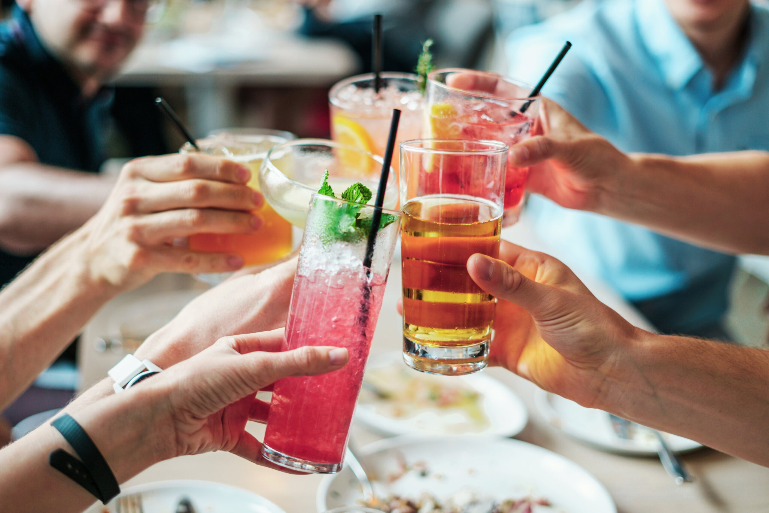 A group of people saying cheers with a selection of different cocktail glasses.