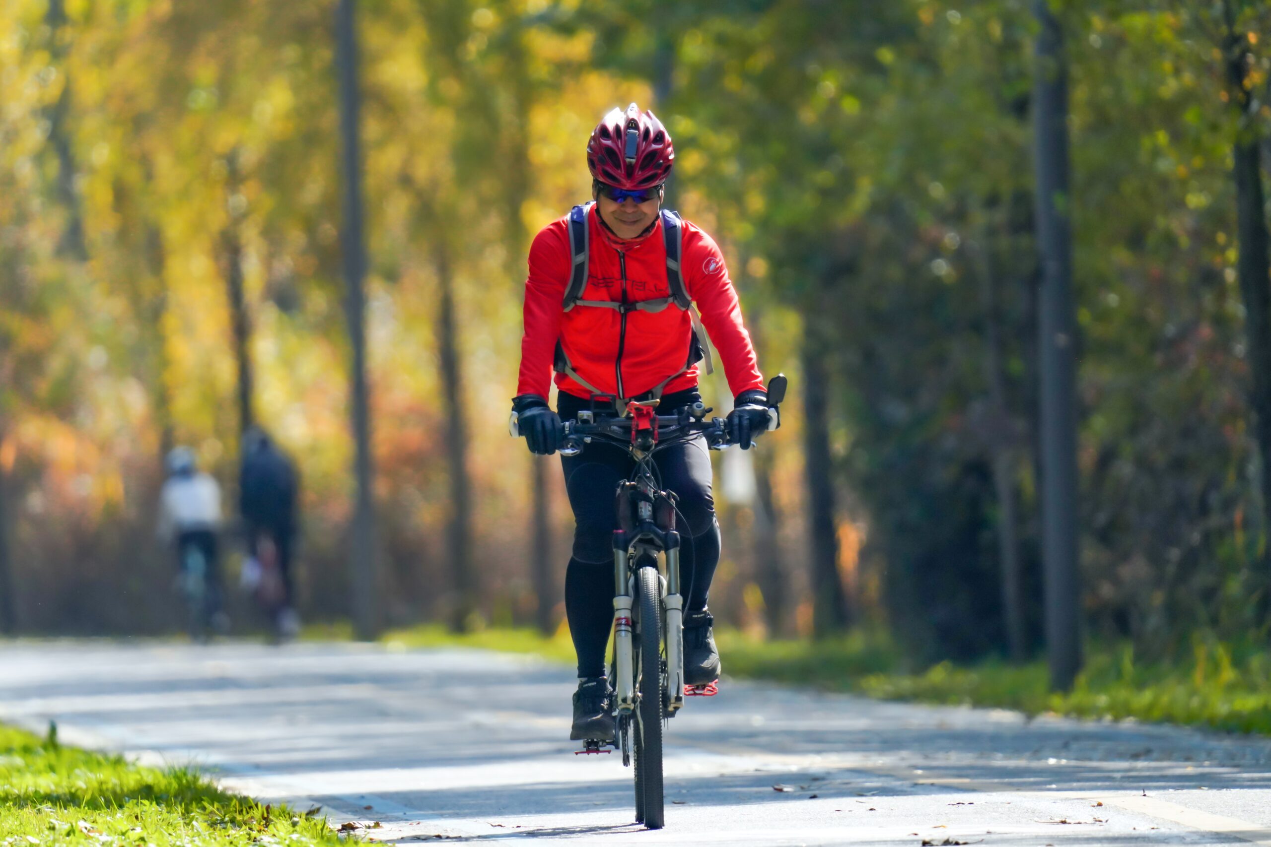 Solo cyclist cycling on the road wearing a protective helmet and an orange jersey.