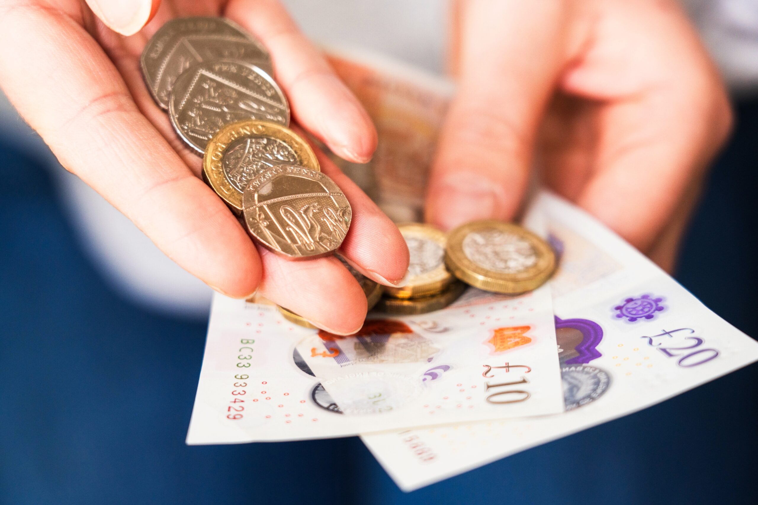 A photograph showing a selection of British monies being held in a person's hand including a twenty and ten pound note plus some coins.