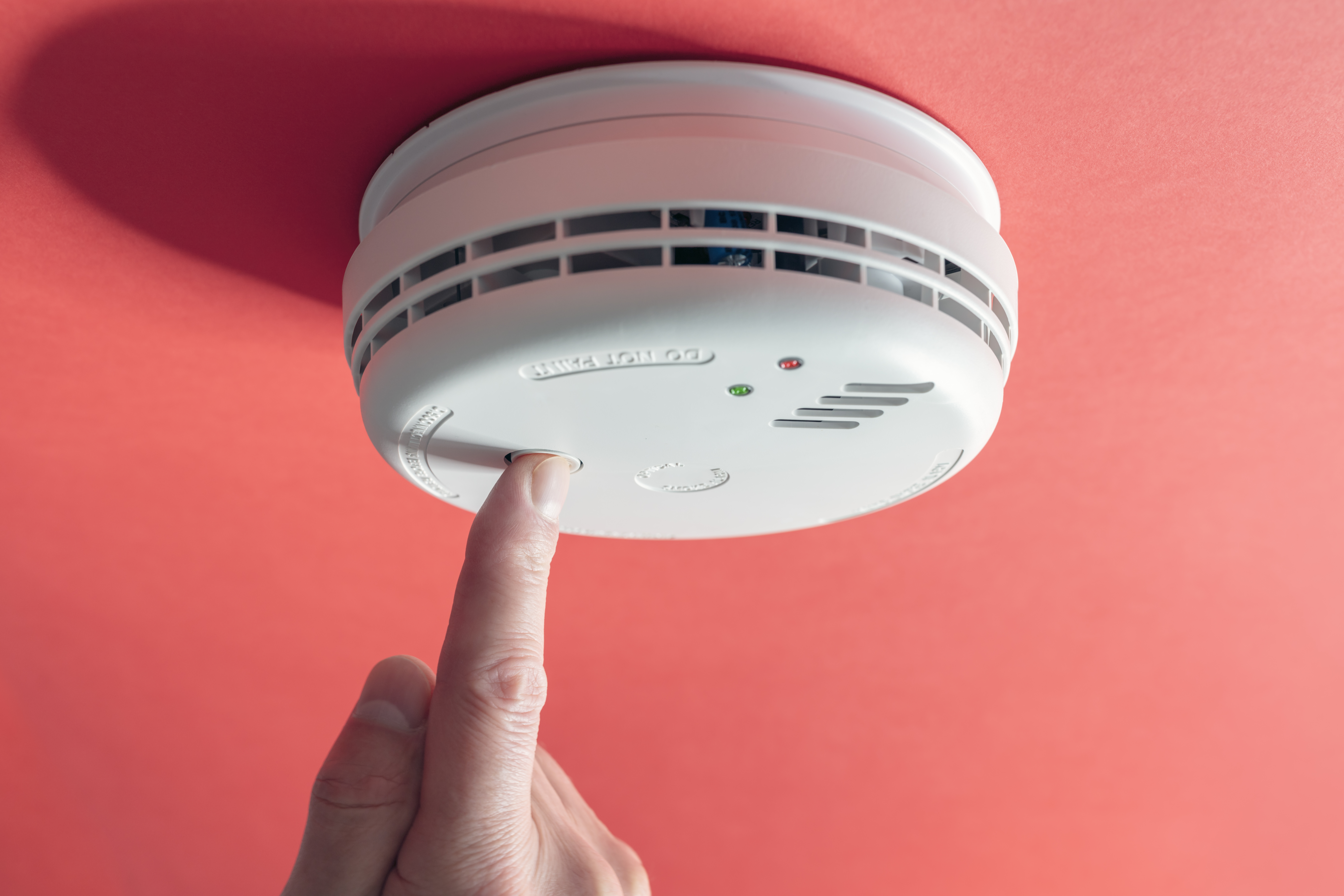 Photograph of smoke alarm with a finger pressing the button
