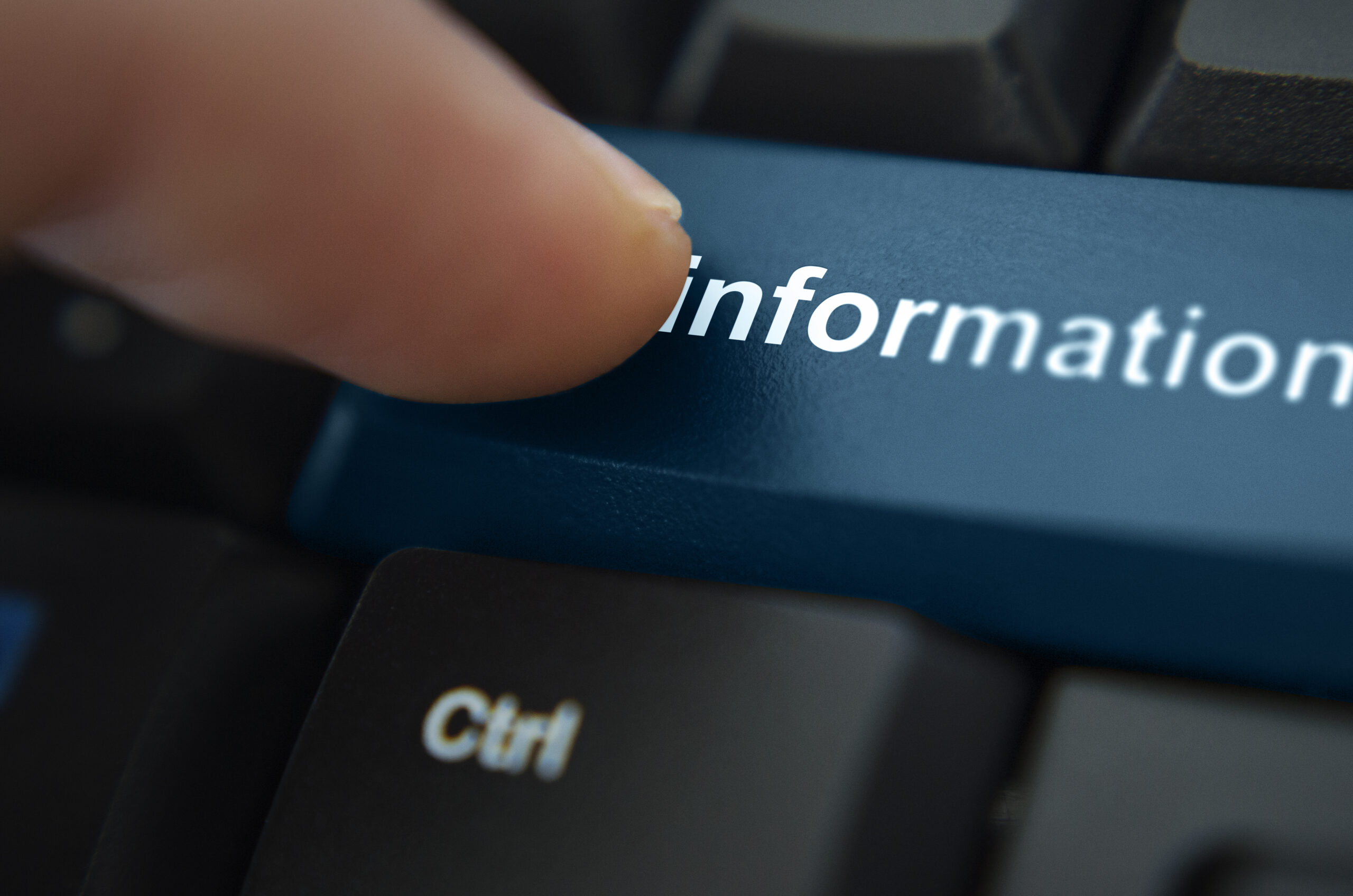A close up of a computer keyboard with a finger pressing a button with the word information written in white font on a blue button.