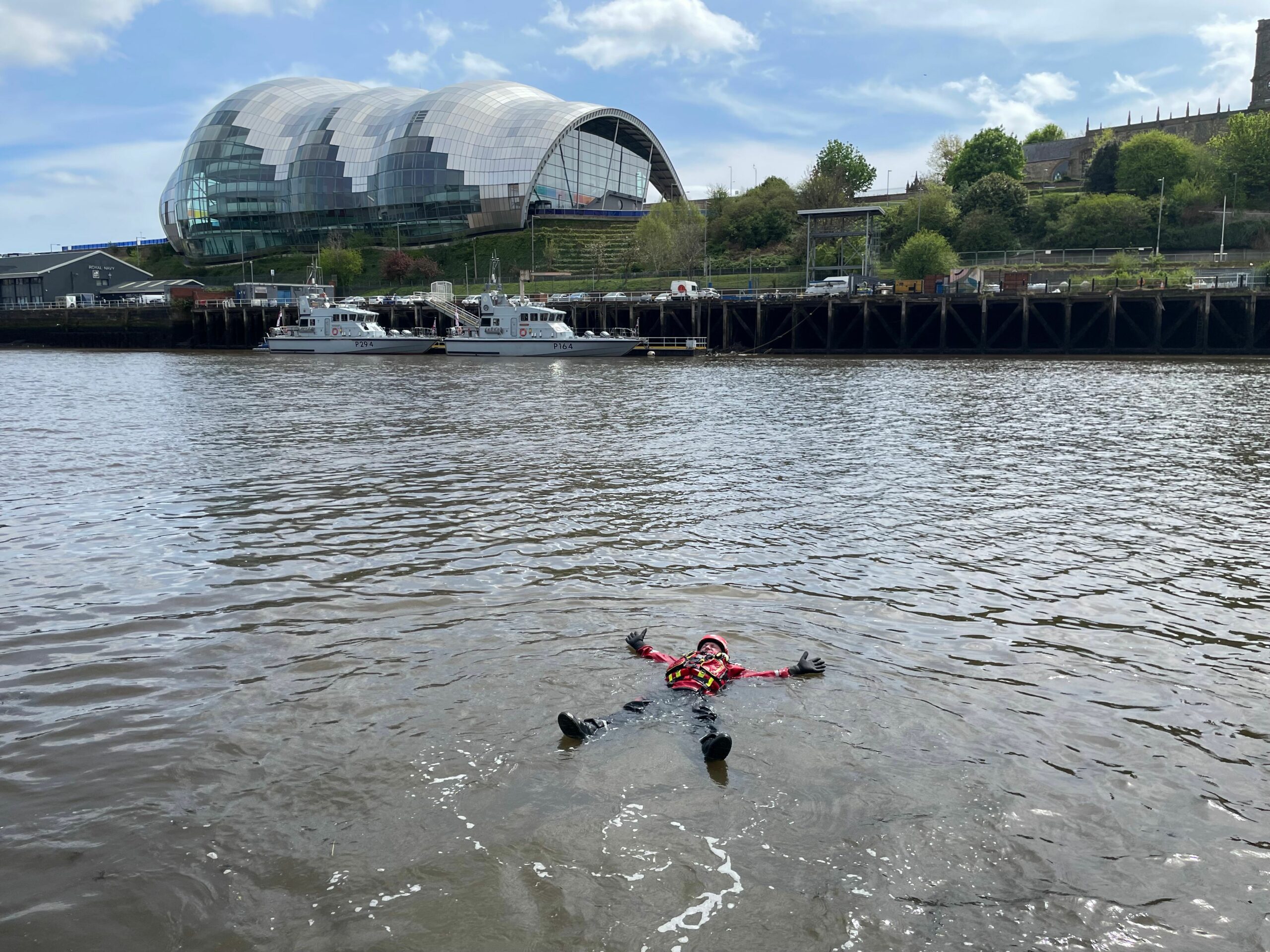 Firefighter floating in the River Tyne in Newcastle by leaning back in a star fish position, demonstrating 'float to live' water safety advice.